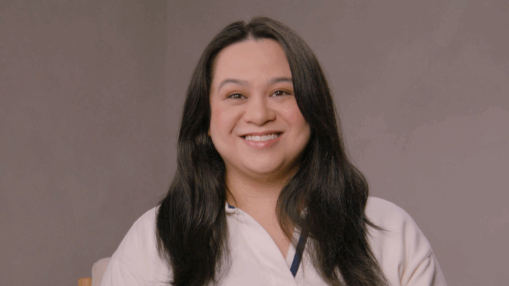 Smiling woman with long dark hair wearing a white top against a neutral background.